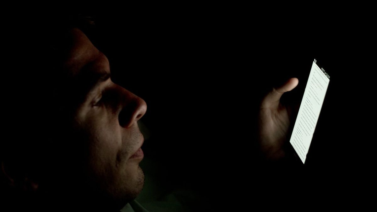 Rosto iluminado pela tela do celular no escuro
